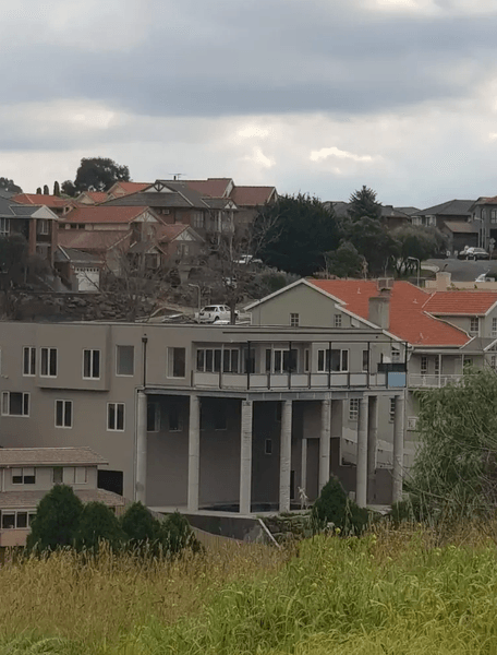 Вид на будинок із нестандартними колонами в Мельбурні, сфотографований здалеку на тлі сусідніх будинків