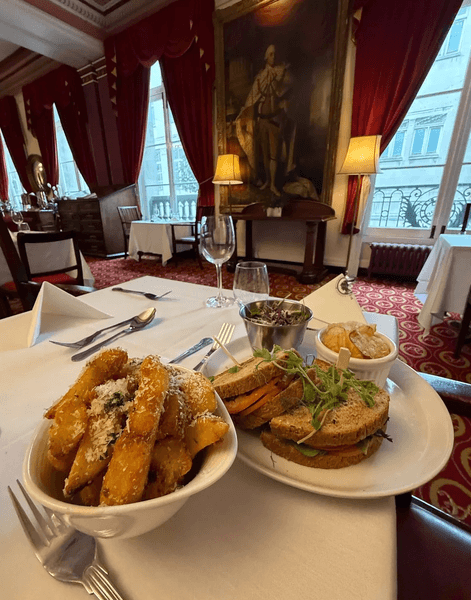 Сэндвич с овощами и порция картофеля фри тройной обжарки подаются на столе в элегантном интерьере ресторана Атенеума