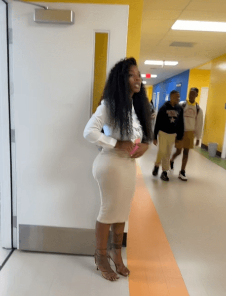 Жінка у світлій спідниці-олівець і блузці стоїть у шкільному коридорі