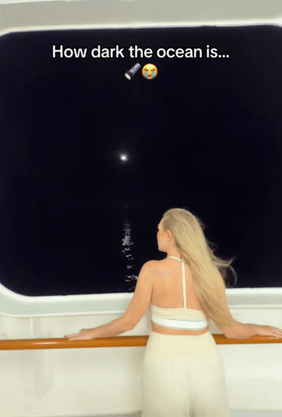 Пасажирка круїзного лайнера дивиться на океан уночі, освітлений лише слабким світлом з корабля