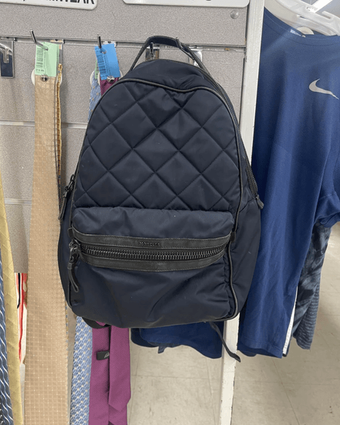 Черный дизайнерский рюкзак Moncler, висит на стенде среди одежды в секонд-хенде