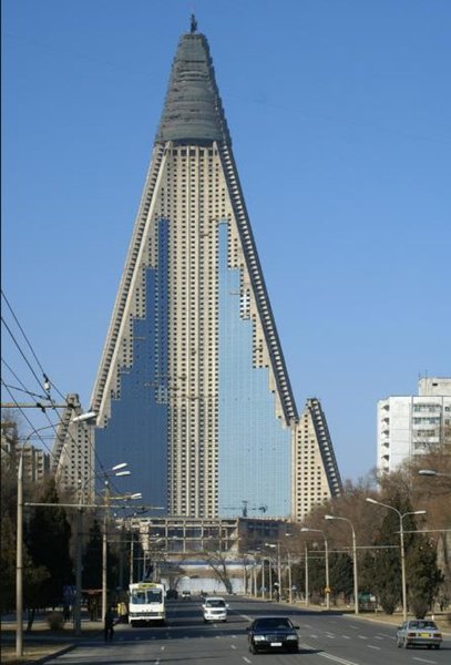 Изглед от улицата към недовършения хотел „Рюгьонг“ в Пхенян, сграда с форма на пирамида и синьо-сива фасада.