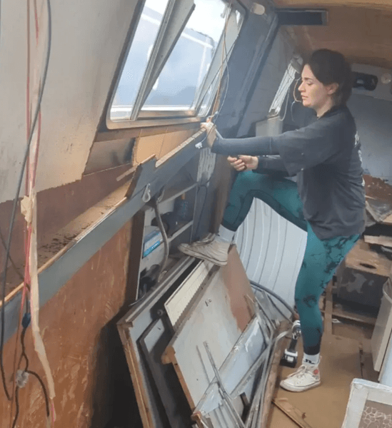 Женщина ремонтирует узкую лодку, превращая старое судно в жилой дом на воде