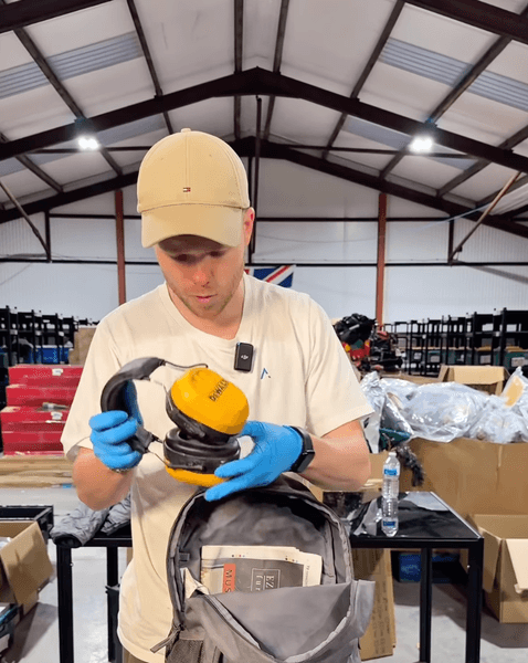 Чоловік у рукавичках оглядає знайдений рюкзак і захисні навушники на складі із втраченим багажем