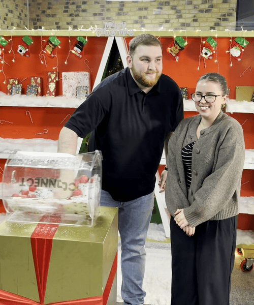 Генеральний директор компанії та співробітниця стоять поруч із лотерейним боксом під час святкового розіграшу подарунків