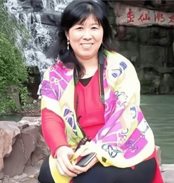 Жена с ярък шал се усмихва, докато седи близо до изкуствен водопад и декоративни камъни.